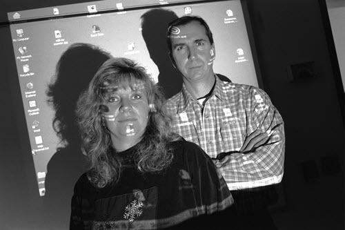 A man and woman pose with icons from a computer screen projected onto them.