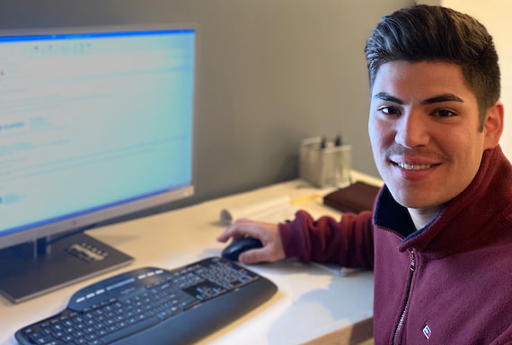 A smiling photo of Alex Padilla, a participant in the Bank's internship program, seated in front of a computer and turned toward the camera.