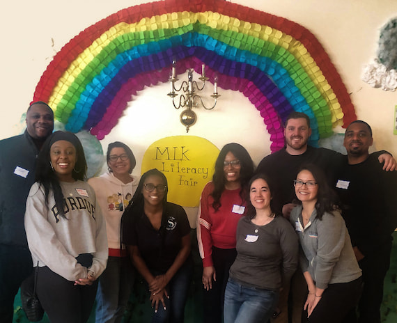 A group of volunteers who facilitated games and activities as part AmeriCorp’s MLK Day of Service event pose under a rainbow decoration.