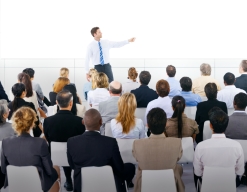 Seated people listening while a man at the front of the room is speaking.